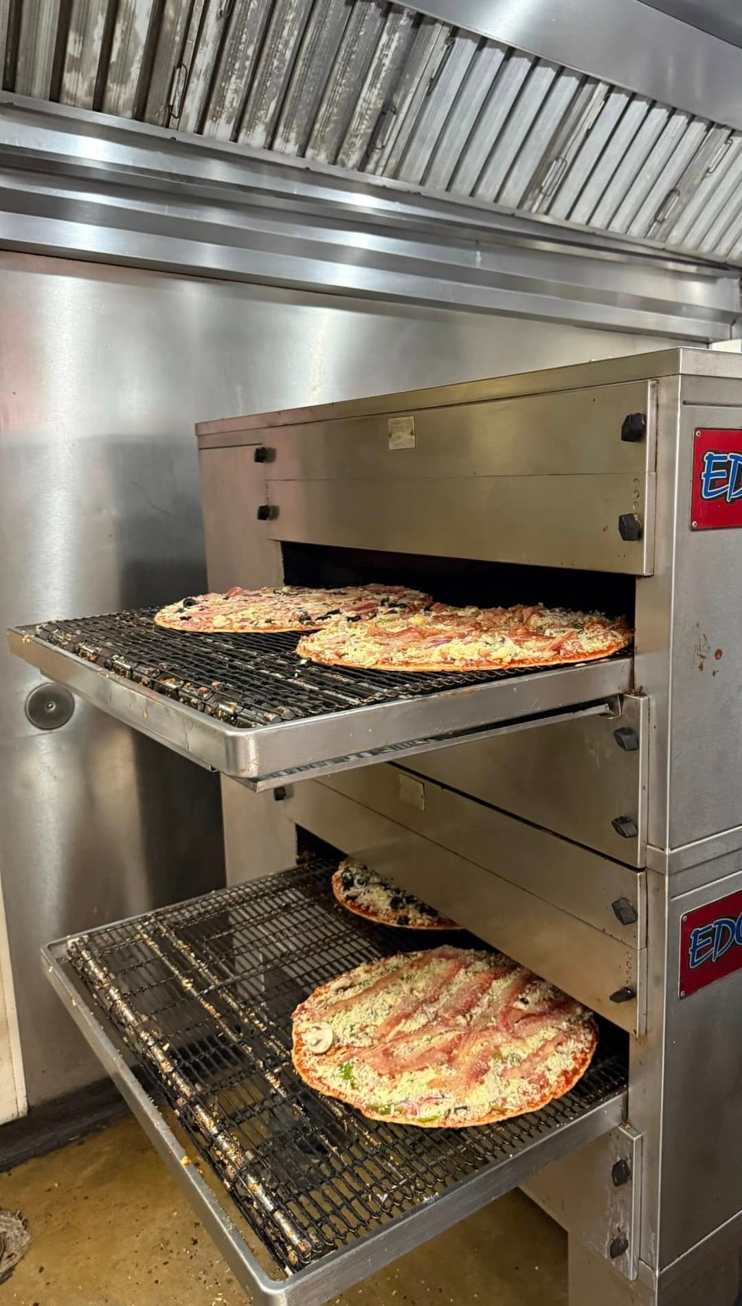 Pizza baking in a commercial oven with multiple trays stacked for cooking.