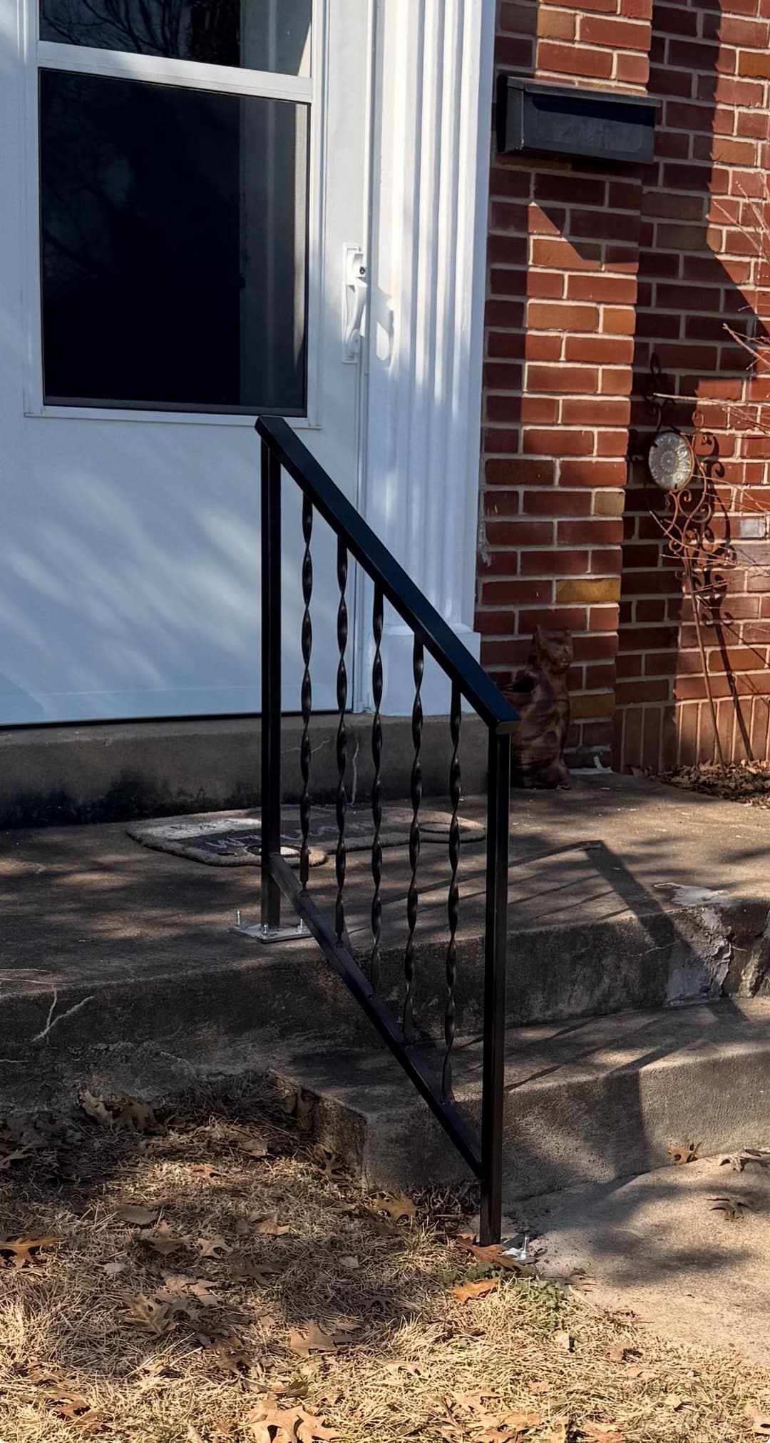 Black metal handrail on brick house steps with a door and decorative features.