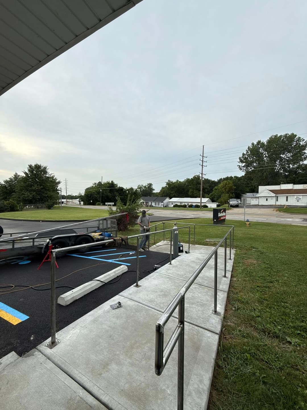 Man adjusting landscaping near accessible ramp and trailer in overcast outdoor setting.