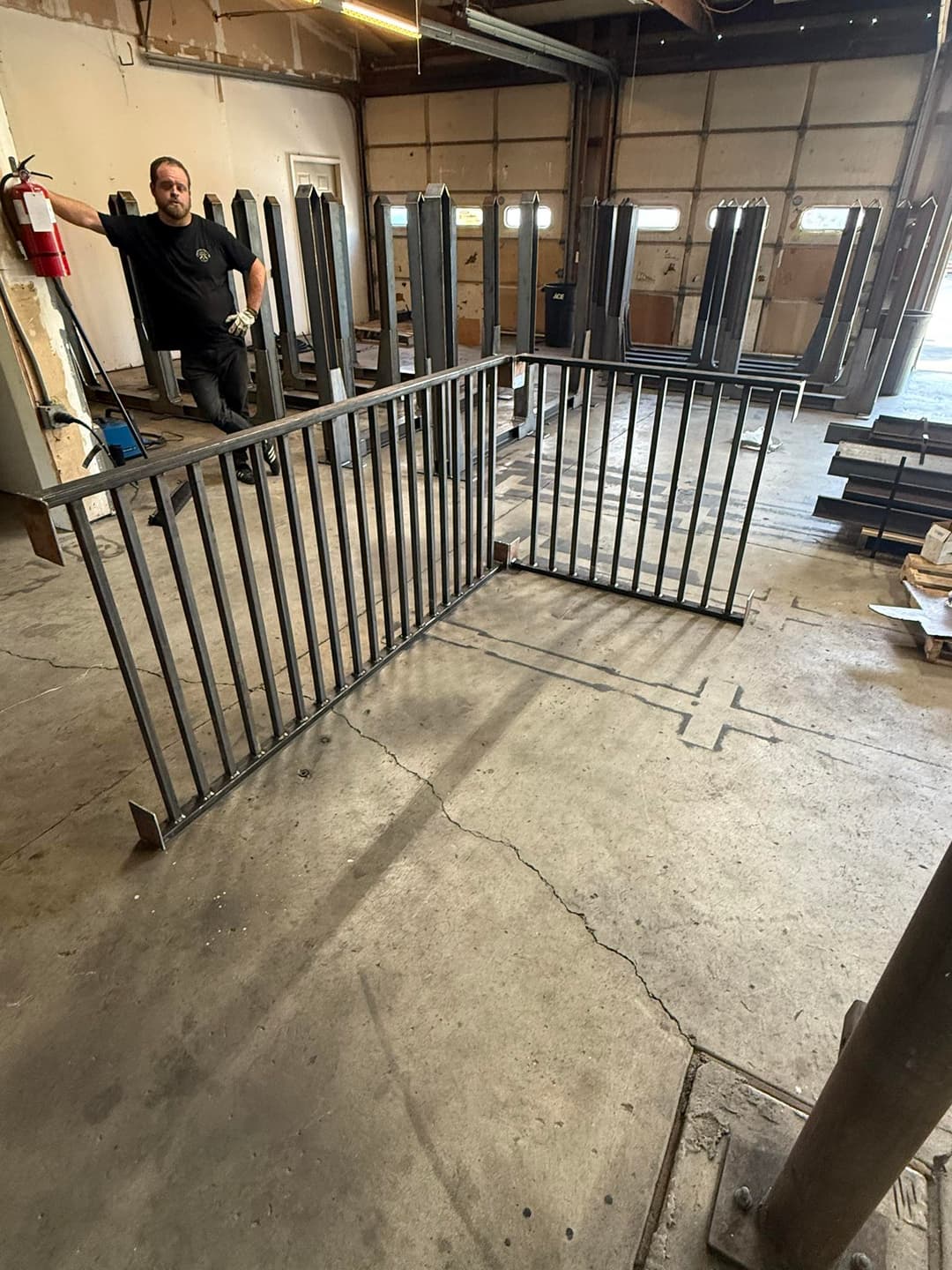 Worker standing beside a metal railing in a workshop with equipment in the background.