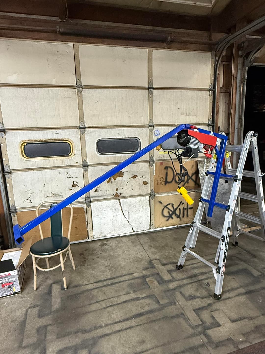 Modified ladder setup with a blue arm and yellow handle, resting against a garage wall.