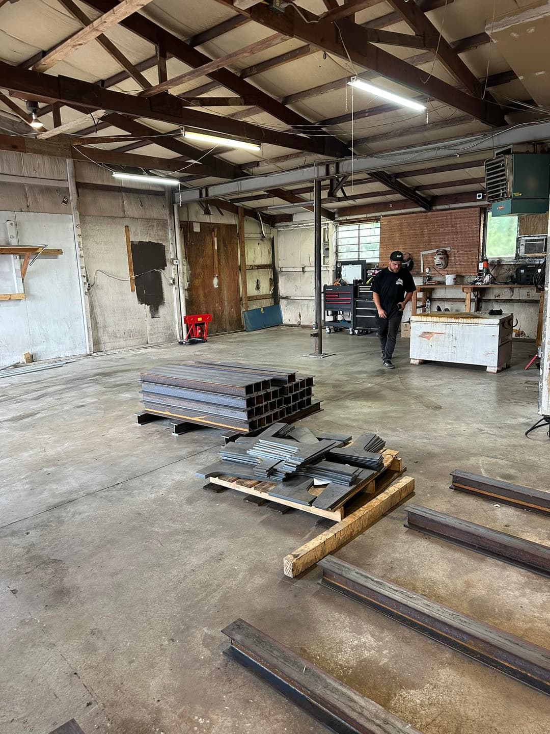 Industrial workshop interior with stacked steel beams and a worker in the background.