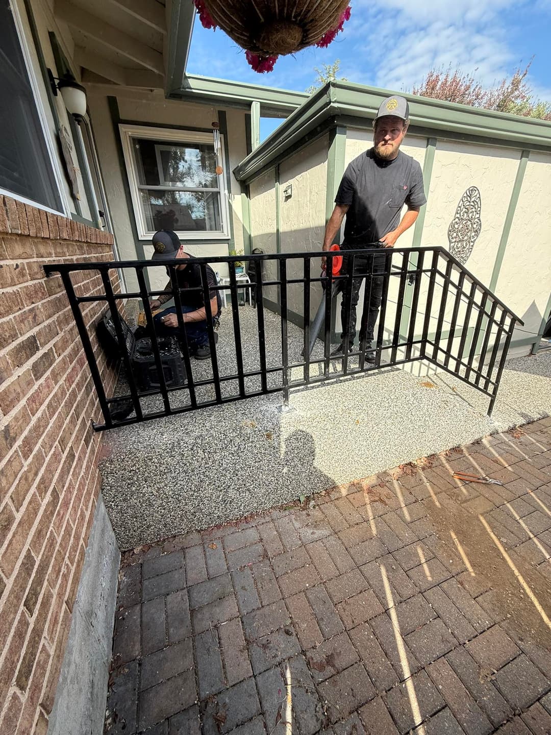 Home renovation with workers installing a black metal railing on textured concrete surface.