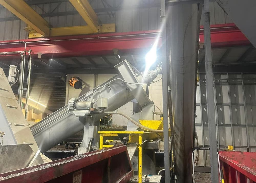 Industrial machinery in a factory, featuring a large auger and metal conveyor system.