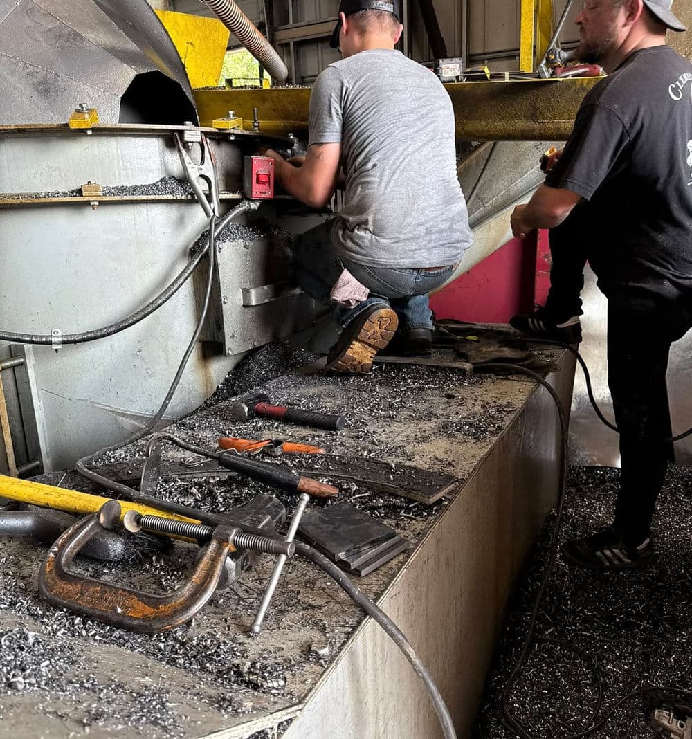 Workers repairing industrial equipment in a workshop with tools scattered on the surface.