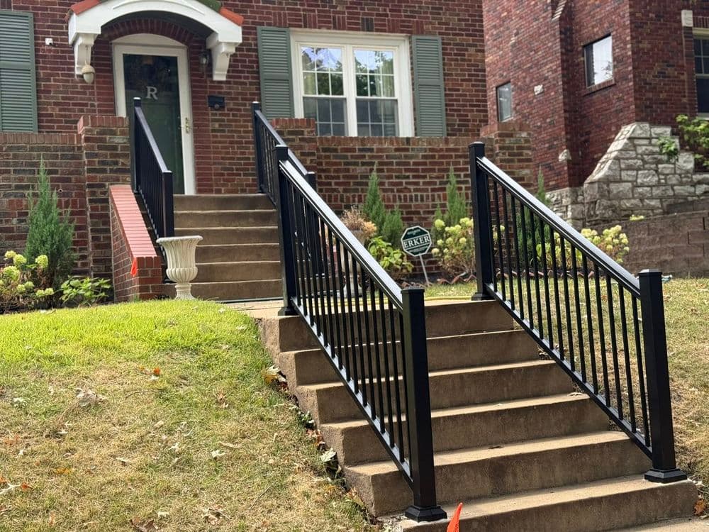 Brick house with landscaped yard and black railing staircase leading to front door.