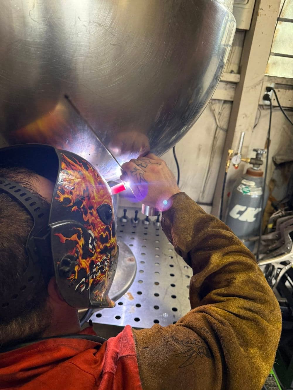 Welder using TIG welding technique on metal with protective gear and safety equipment.