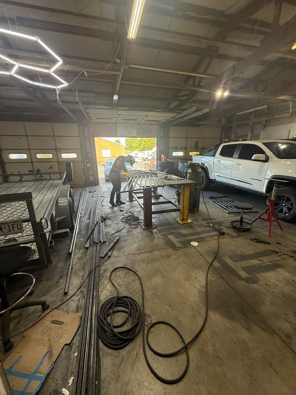 Worker fabricating metal structures in a well-lit workshop with tools and equipment.
