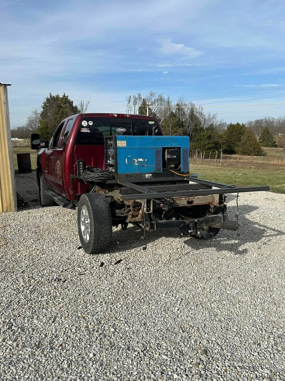 Red pickup truck with flatbed and a blue generator parked on gravel outdoors.
