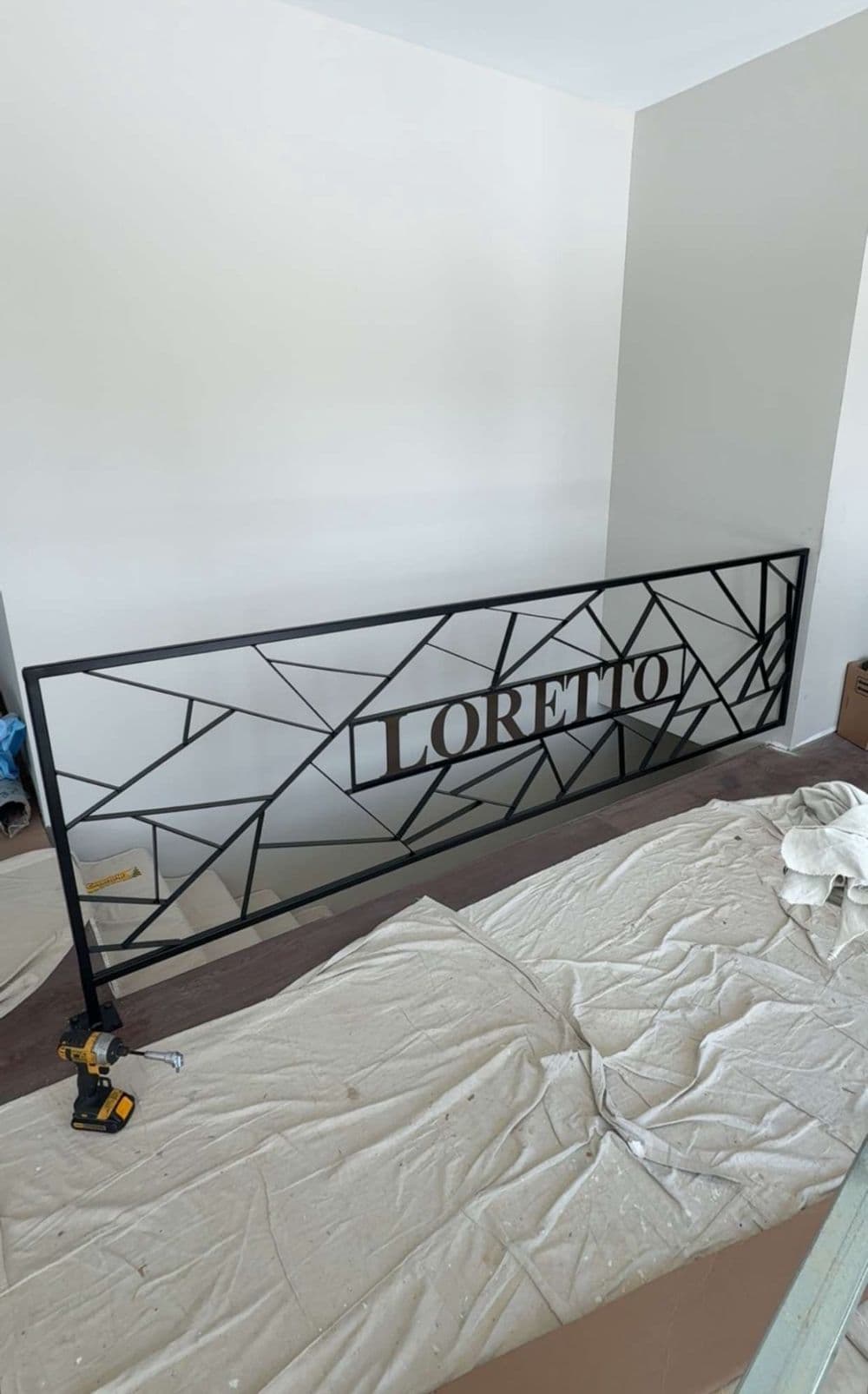 Geometric black railing with "LORETTO" design over a construction site with tools and tarps.